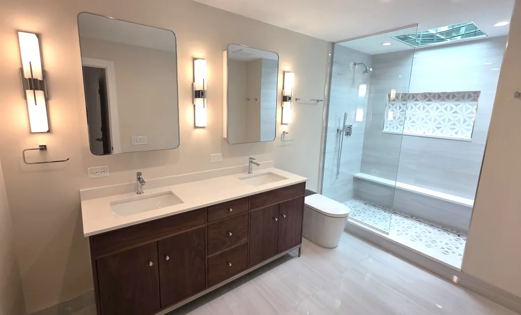 A spacious luxury bathroom layout by Maya Construction showcasing a long double-sink vanity, modern mirrors, and a large curbless walk-in shower with a built-in bench.